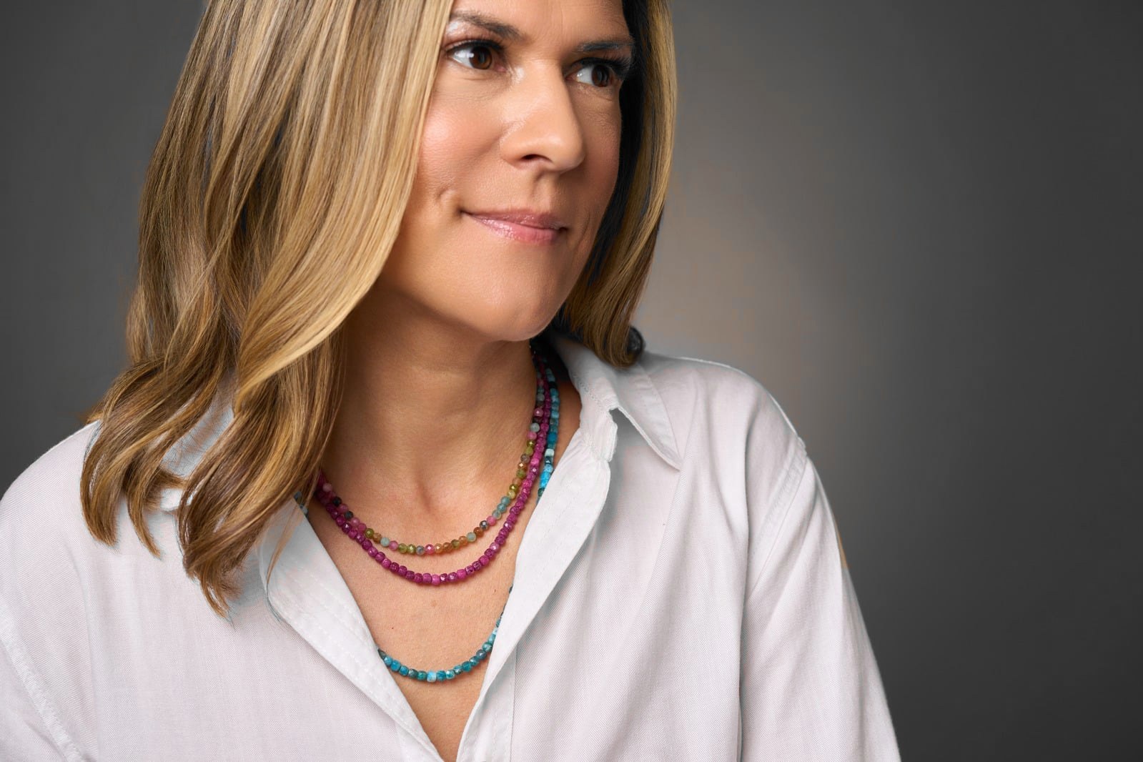 Layered colorful gemstone necklaces worn with a white shirt.