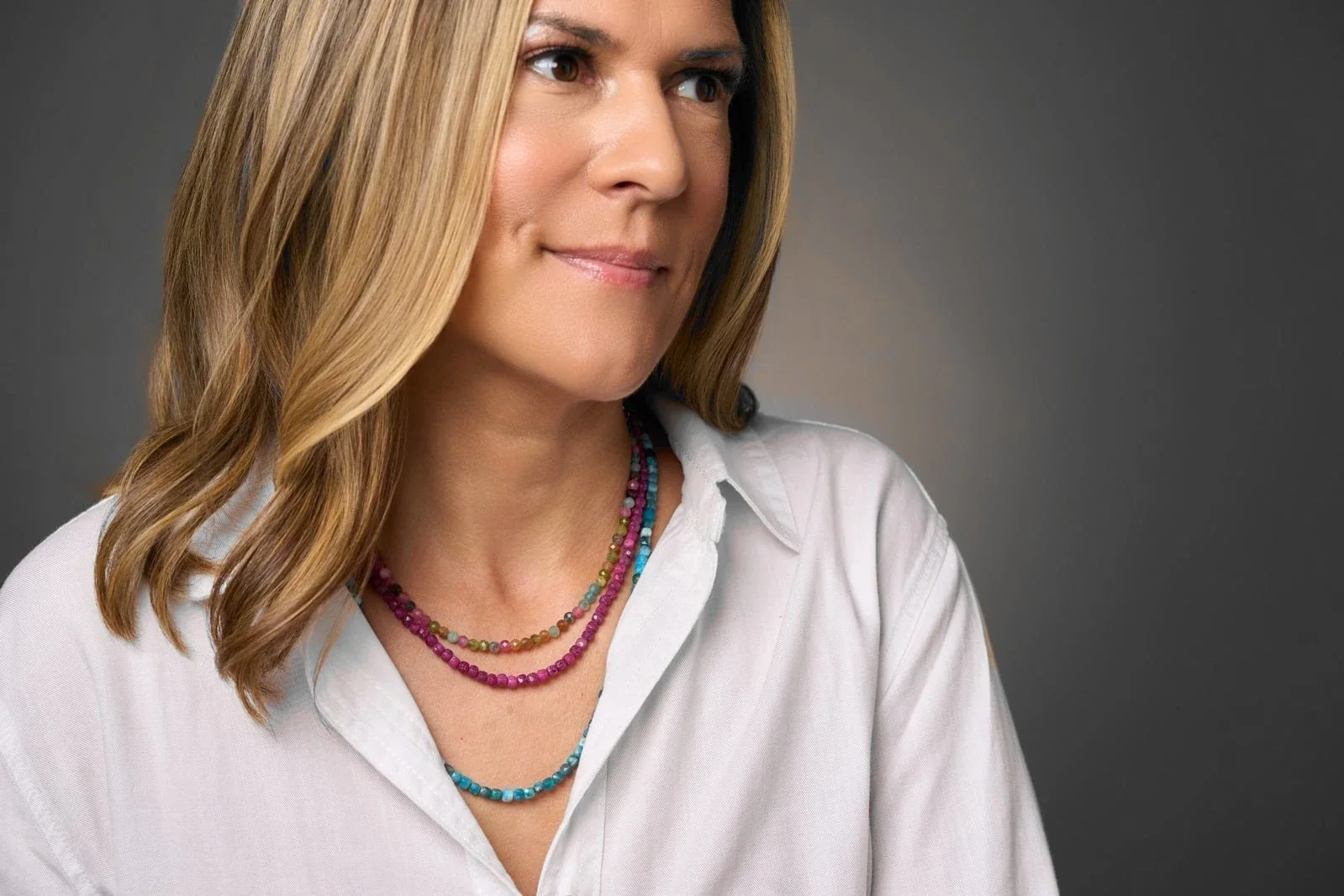 Magda Loczi in a white shirt, wearing layered pink, green and blue gemstone strands.